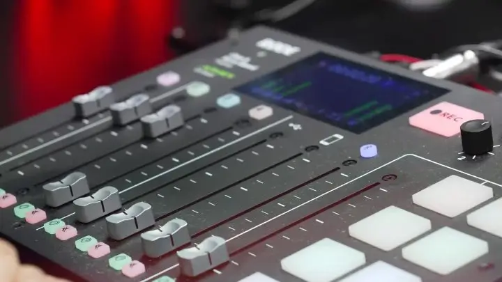 Close-up of a hand adjusting sliders on a digital audio mixer with illuminated buttons and display screen
