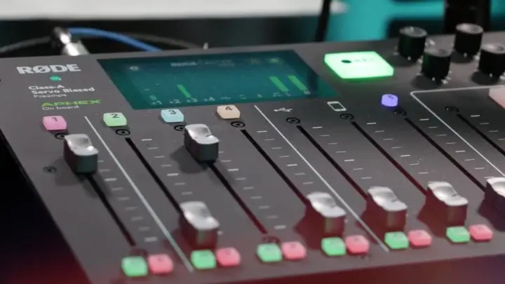 Close-up of a hand adjusting sliders on a digital audio mixer with illuminated buttons and display screen