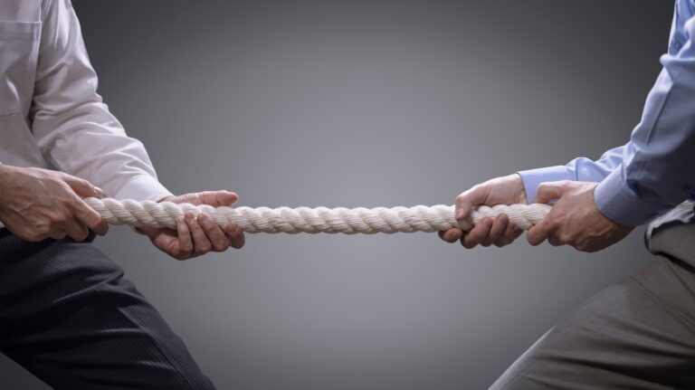 Two men in business attire playing tug of war with a rope