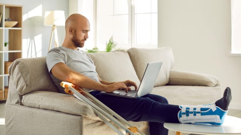man with a cast on his leg sitting with a laptop