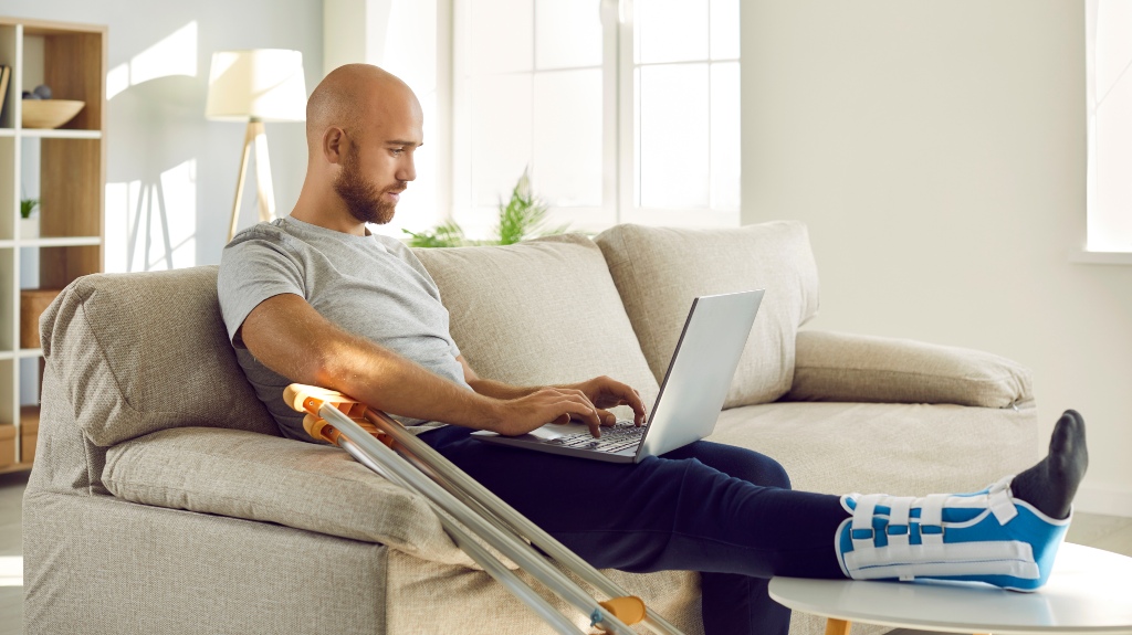 man with a cast on his leg sitting with a laptop