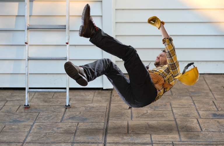 A worker in a hard hat falls from a ladder onto a concrete floor