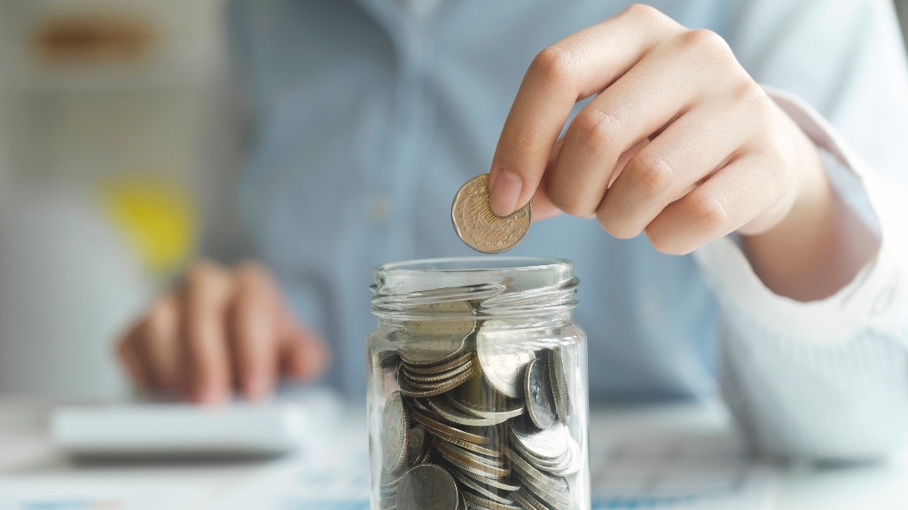 Woman hand putting coin on saving jar