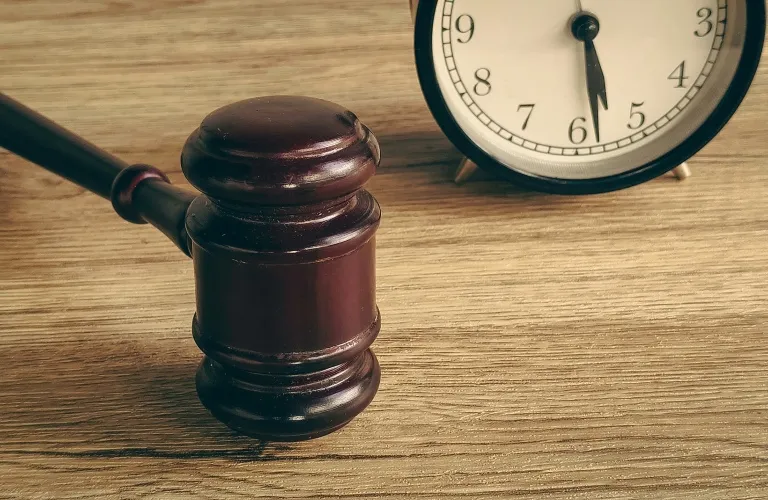 Wooden judge's gavel and round clock showing 6:30 on a wooden surface.
