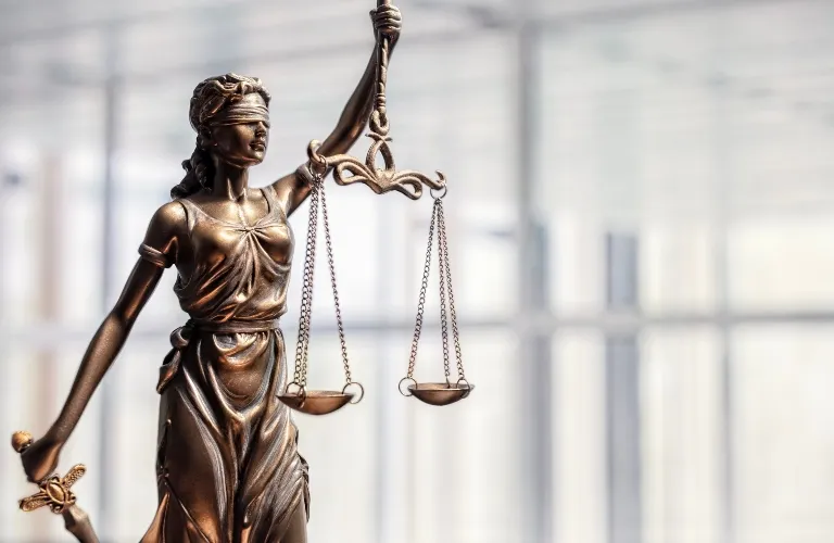 Bronze statue of Lady Justice blindfolded, holding scales and a sword, against a blurred background.