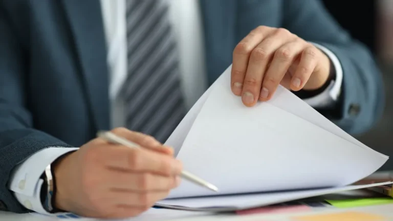 Business professional in suit reviewing and writing on documents at desk.