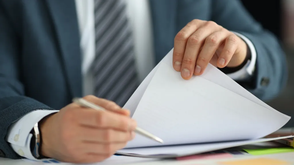 Business professional in suit reviewing and writing on documents at desk.