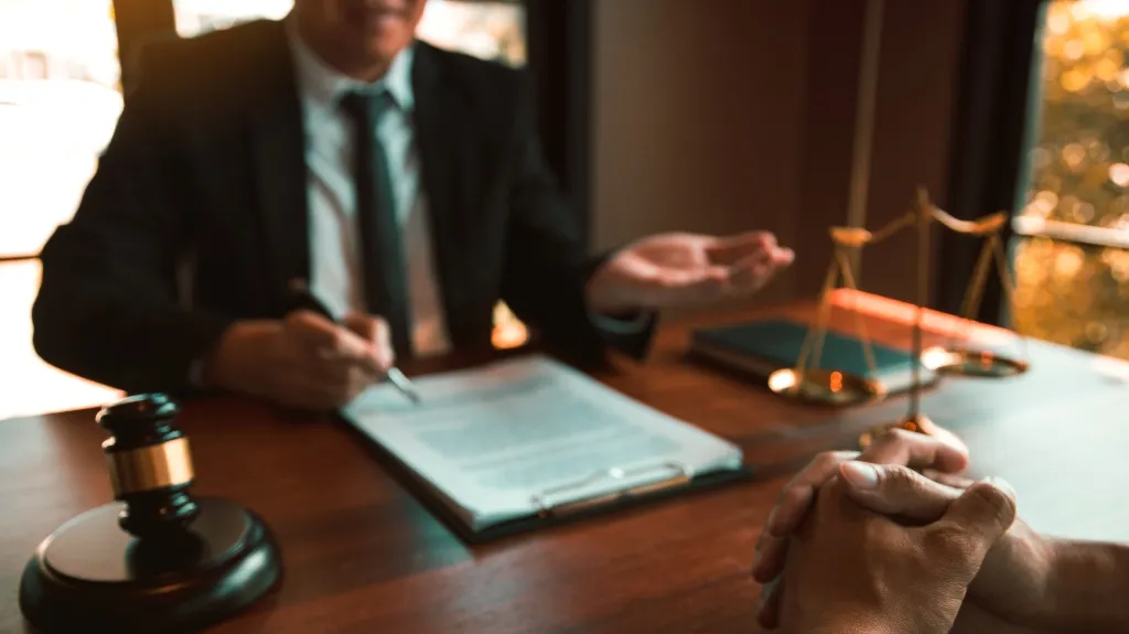Two individuals in a legal consultation with a gavel and scales of justice on a wooden desk.