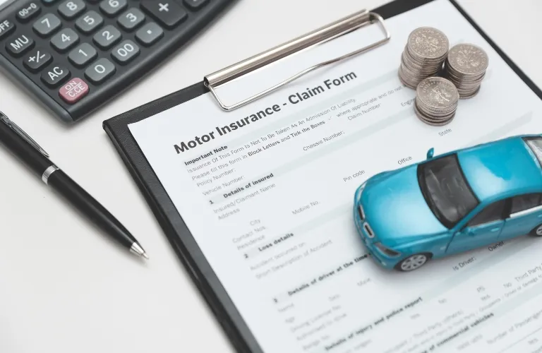 Motor insurance claim form on clipboard with pen, calculator, coins, and toy car.