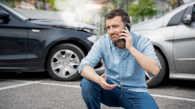 Man in blue shirt making a phone call near two damaged cars after an accident.