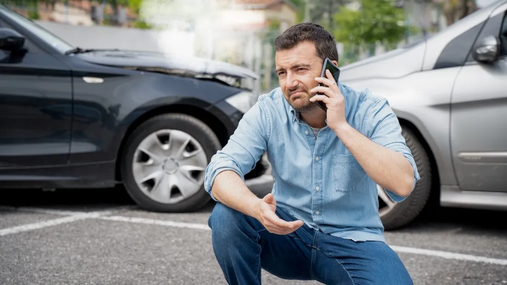 Man in blue shirt making a phone call near two damaged cars after an accident.