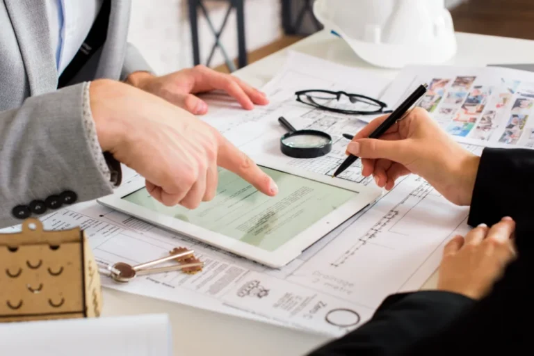 Two professionals reviewing architectural plans and digital documents on a tablet at a desk.