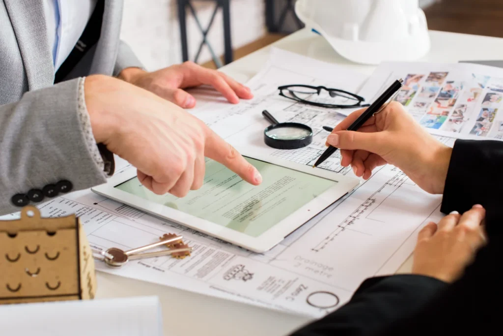 Two professionals reviewing architectural plans and digital documents on a tablet at a desk.